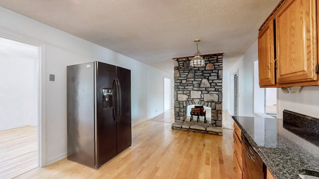 kitchen featuring pendant lighting, dark stone counters, light hardwood / wood-style floors, black fridge with ice dispenser, and a textured ceiling