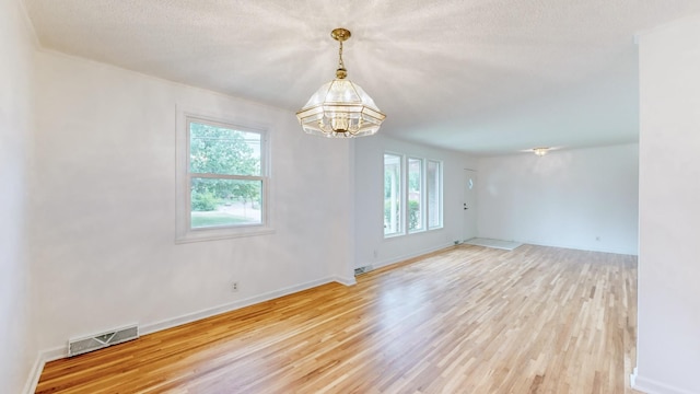 empty room with a notable chandelier, a textured ceiling, and light hardwood / wood-style flooring