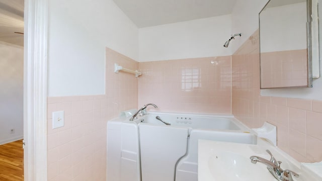 bathroom with hardwood / wood-style flooring, a tub to relax in, sink, and tile walls