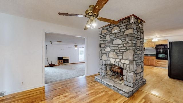 unfurnished living room featuring ceiling fan, a stone fireplace, and light wood-type flooring