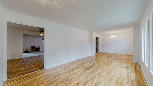 empty room featuring ceiling fan with notable chandelier, light hardwood / wood-style flooring, a textured ceiling, and plenty of natural light