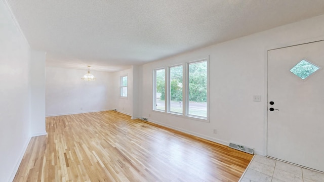 entrance foyer featuring light hardwood / wood-style floors, a textured ceiling, and a notable chandelier