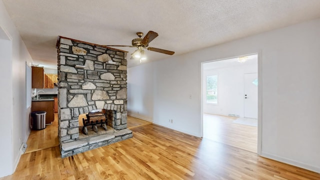 living room featuring sink, light hardwood / wood-style flooring, ceiling fan, a textured ceiling, and a stone fireplace