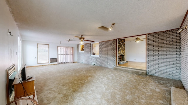 unfurnished living room featuring ceiling fan, brick wall, carpet flooring, and a textured ceiling