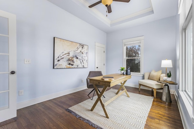 home office with dark wood-type flooring, ceiling fan, and a tray ceiling