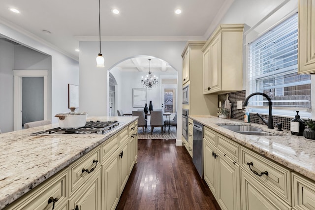 kitchen featuring sink, light stone counters, hanging light fixtures, appliances with stainless steel finishes, and cream cabinetry