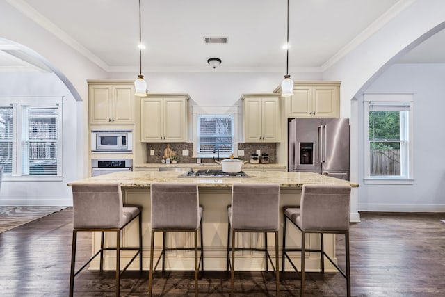 kitchen featuring appliances with stainless steel finishes, light stone counters, cream cabinets, and decorative light fixtures