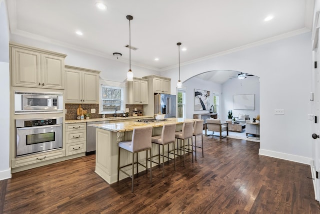 kitchen featuring a kitchen island, appliances with stainless steel finishes, pendant lighting, light stone countertops, and cream cabinetry