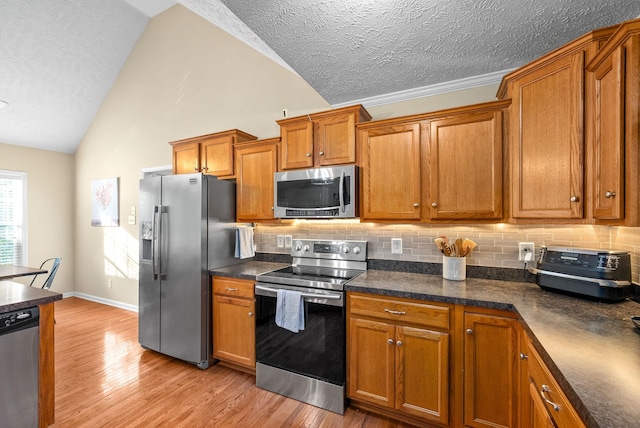 kitchen featuring vaulted ceiling, appliances with stainless steel finishes, backsplash, and light hardwood / wood-style flooring