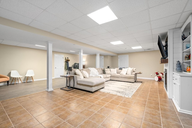 living room with a drop ceiling, light tile patterned floors, and decorative columns