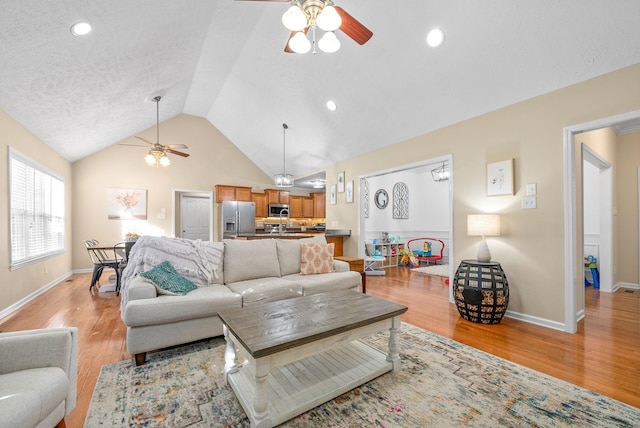 living room with vaulted ceiling, a textured ceiling, ceiling fan, and light hardwood / wood-style floors