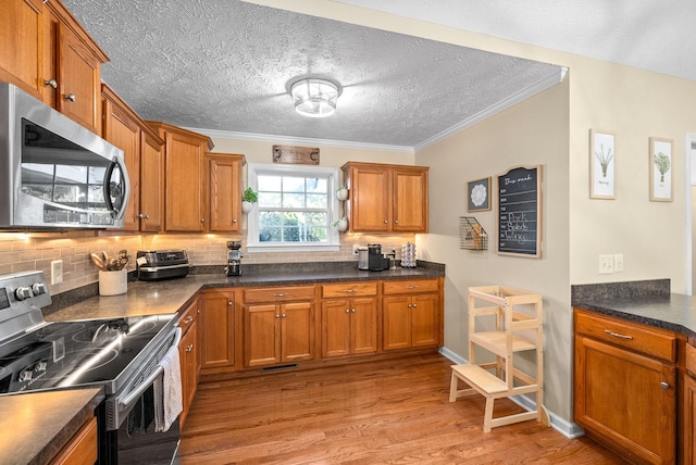 kitchen with a textured ceiling, light wood-type flooring, ornamental molding, appliances with stainless steel finishes, and backsplash