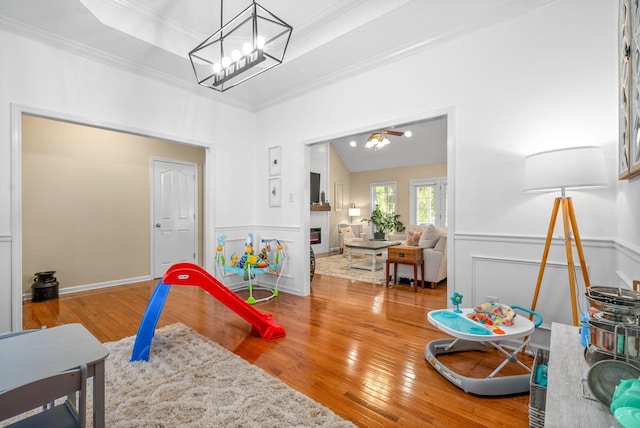 playroom featuring vaulted ceiling, hardwood / wood-style flooring, ornamental molding, a notable chandelier, and a raised ceiling