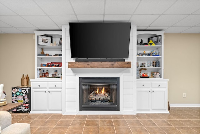 tiled living room with a drop ceiling, built in shelves, and a large fireplace