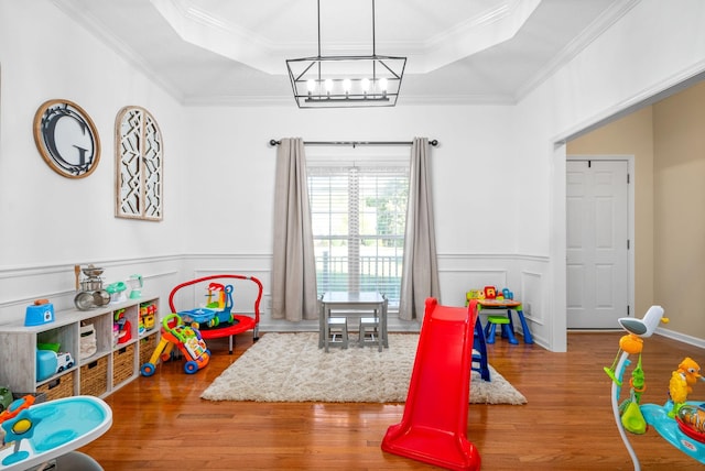 recreation room with an inviting chandelier, ornamental molding, wood-type flooring, and a raised ceiling