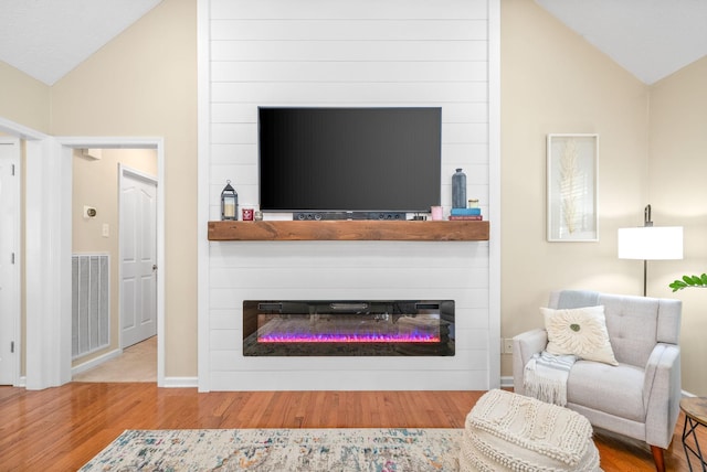 living room featuring hardwood / wood-style flooring, lofted ceiling, and a large fireplace