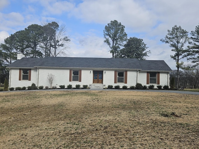 ranch-style home featuring a front yard, french doors, brick siding, and a chimney