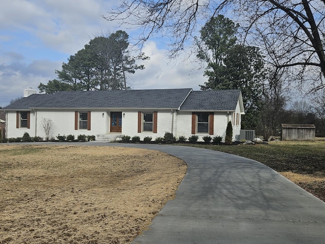 view of front of house with brick siding, roof with shingles, curved driveway, and a chimney