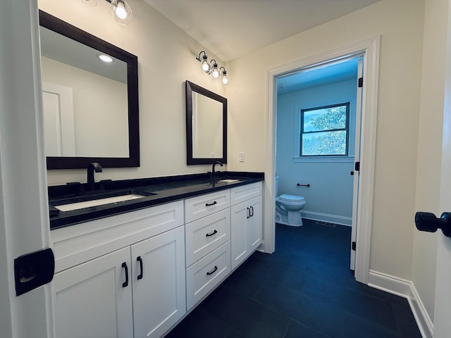 bathroom featuring double vanity, toilet, baseboards, and a sink