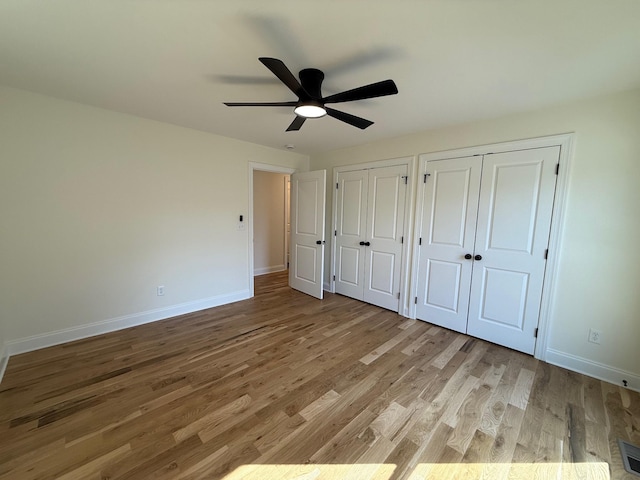 unfurnished bedroom featuring ceiling fan, baseboards, two closets, and wood finished floors