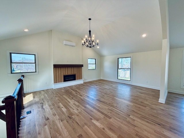 unfurnished living room with lofted ceiling, a fireplace, light wood-style floors, a notable chandelier, and a wall mounted AC