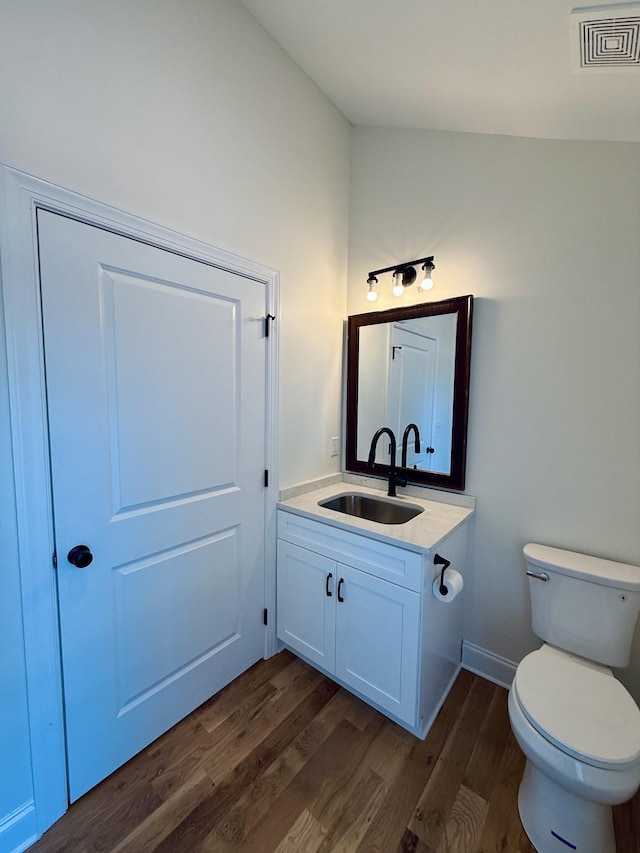 half bath featuring vanity, wood finished floors, visible vents, vaulted ceiling, and toilet