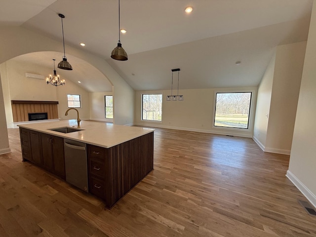 kitchen with wood finished floors, a sink, dark brown cabinets, stainless steel dishwasher, and open floor plan