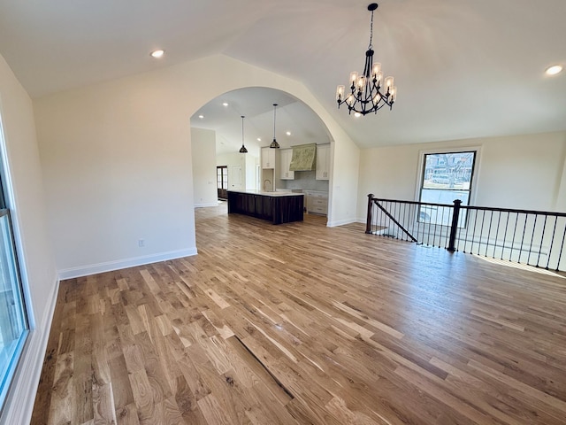 unfurnished room featuring baseboards, light wood-style floors, a chandelier, and arched walkways