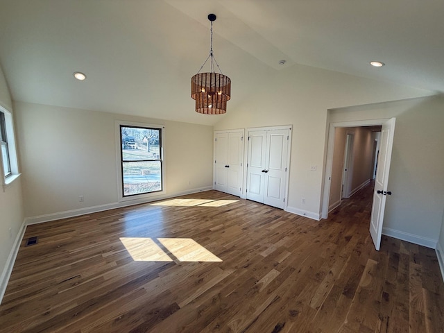 unfurnished bedroom with visible vents, two closets, dark wood-style floors, and vaulted ceiling