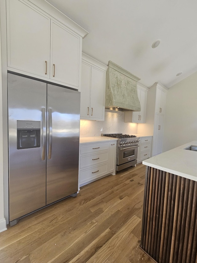 kitchen with light wood finished floors, light countertops, custom range hood, appliances with stainless steel finishes, and white cabinetry