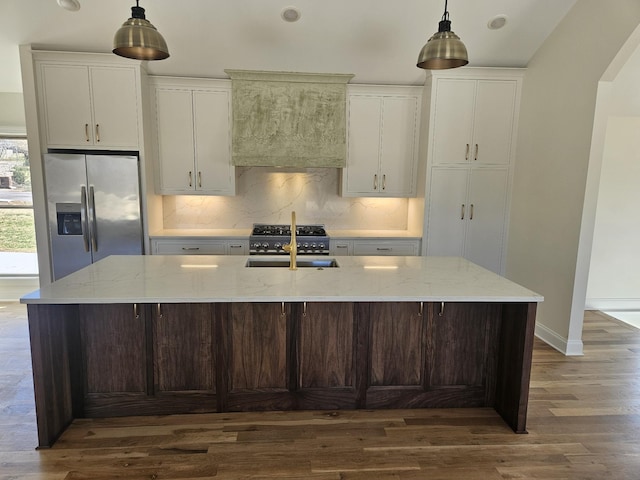 kitchen with arched walkways, a sink, a large island, stainless steel refrigerator with ice dispenser, and tasteful backsplash