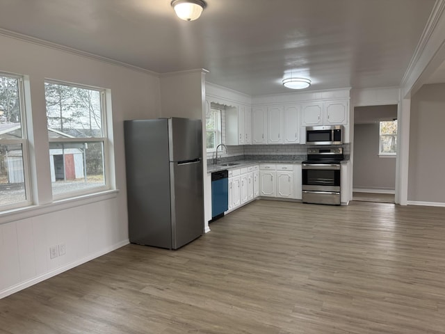 kitchen with sink, hardwood / wood-style flooring, white cabinetry, stainless steel appliances, and ornamental molding