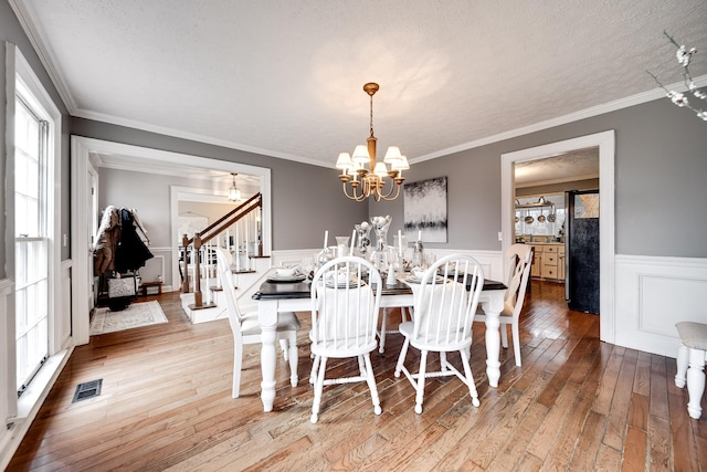 dining space with an inviting chandelier, crown molding, a textured ceiling, and light wood-type flooring