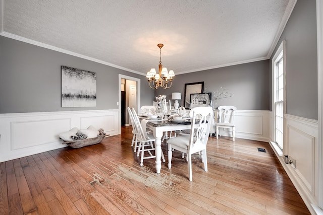 dining space with an inviting chandelier, crown molding, wood-type flooring, and a textured ceiling