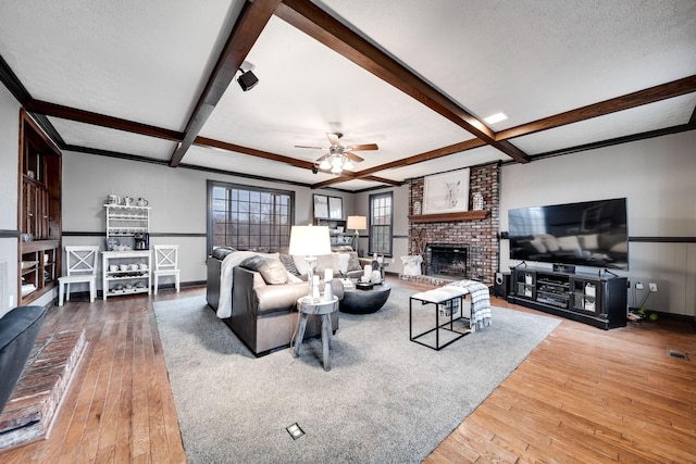 living room featuring beamed ceiling, wood-type flooring, a brick fireplace, and a textured ceiling