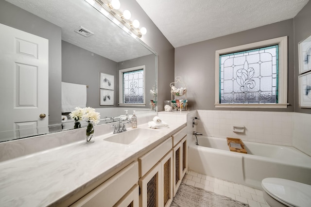 bathroom with tile patterned flooring, a bathtub, vanity, a textured ceiling, and toilet