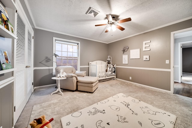 bedroom with carpet, ceiling fan, a crib, crown molding, and a textured ceiling