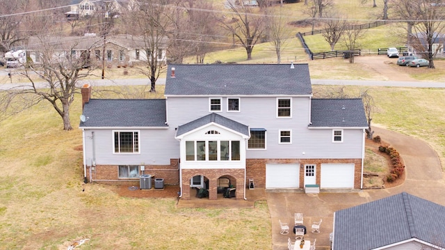 back of property with central AC unit, a garage, and a yard