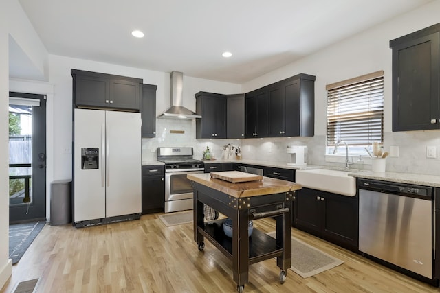 kitchen featuring wall chimney exhaust hood, sink, light stone counters, stainless steel appliances, and light hardwood / wood-style floors