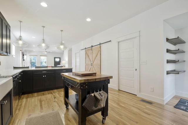 kitchen with decorative light fixtures, dishwasher, light hardwood / wood-style floors, kitchen peninsula, and a barn door