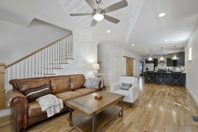 living room with ceiling fan, a barn door, and light wood-type flooring