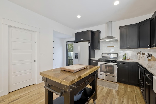 kitchen featuring wall chimney range hood, light hardwood / wood-style flooring, stainless steel appliances, and light stone countertops