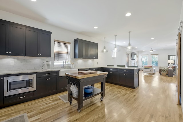 kitchen featuring stainless steel microwave, decorative light fixtures, sink, light stone countertops, and light hardwood / wood-style flooring