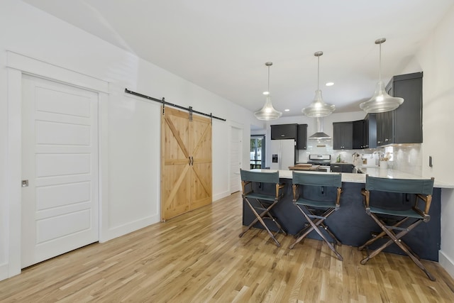 kitchen with refrigerator with ice dispenser, a kitchen bar, kitchen peninsula, a barn door, and wall chimney range hood