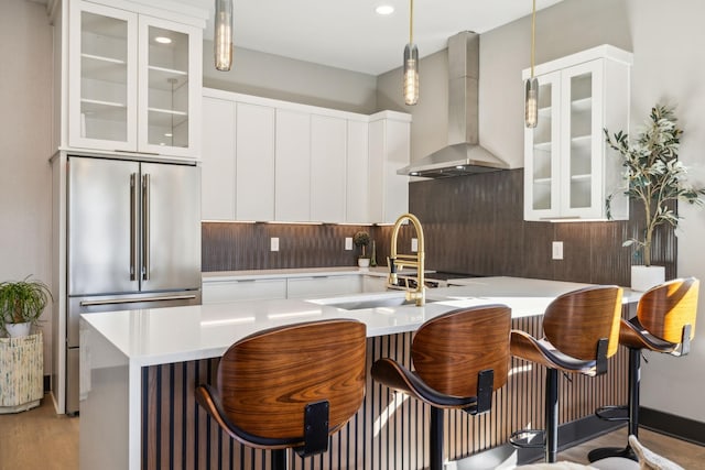 kitchen with wall chimney exhaust hood, a breakfast bar, high end fridge, sink, and hanging light fixtures