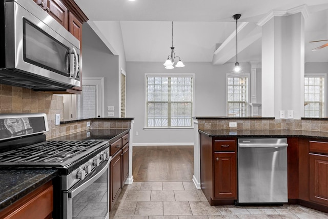 kitchen featuring lofted ceiling, appliances with stainless steel finishes, hanging light fixtures, decorative backsplash, and dark stone counters