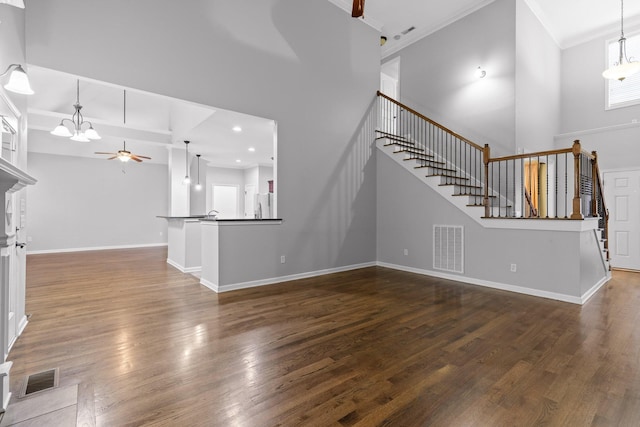 unfurnished living room featuring ornamental molding, dark hardwood / wood-style floors, ceiling fan with notable chandelier, and a towering ceiling