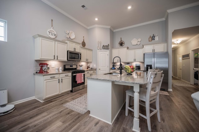 kitchen featuring sink, white cabinetry, stainless steel appliances, light stone countertops, and a kitchen island with sink