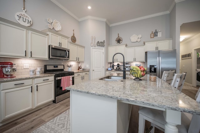 kitchen with an island with sink, sink, ornamental molding, light stone counters, and stainless steel appliances