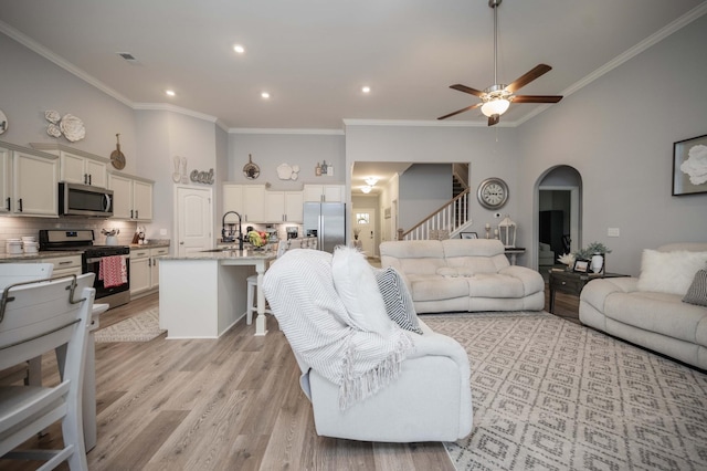 living room featuring sink, ornamental molding, ceiling fan, light hardwood / wood-style floors, and a high ceiling